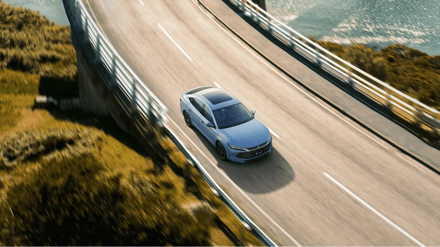 Car driving on a winding road with scenic mountains and water in the background